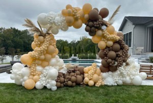 Autumn colors balloon art arch by an outdoor swimming pool